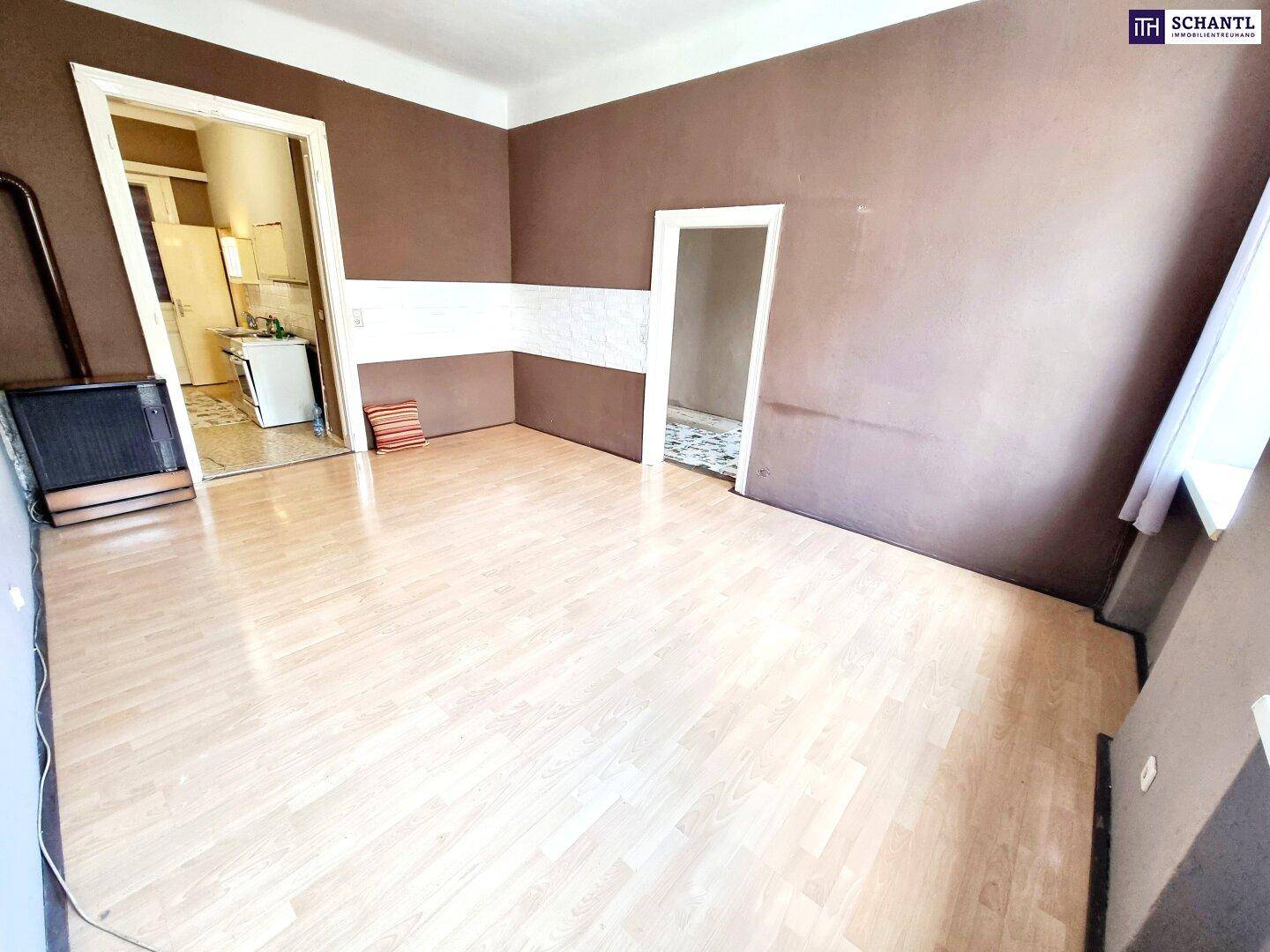 Geräumiges Zimmer mit Laminatboden und einem Ofen, das den Zugang zu weiteren Räumen ermöglicht.