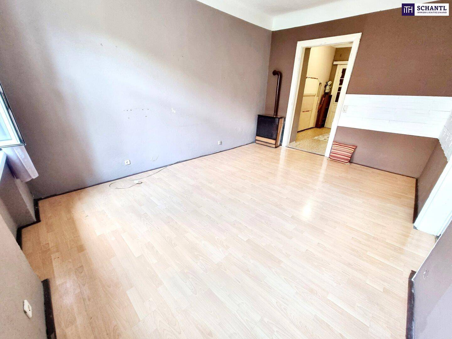 Helles Wohnzimmer mit Laminatboden und einem traditionellen Ofen, bereit zur Renovierung.