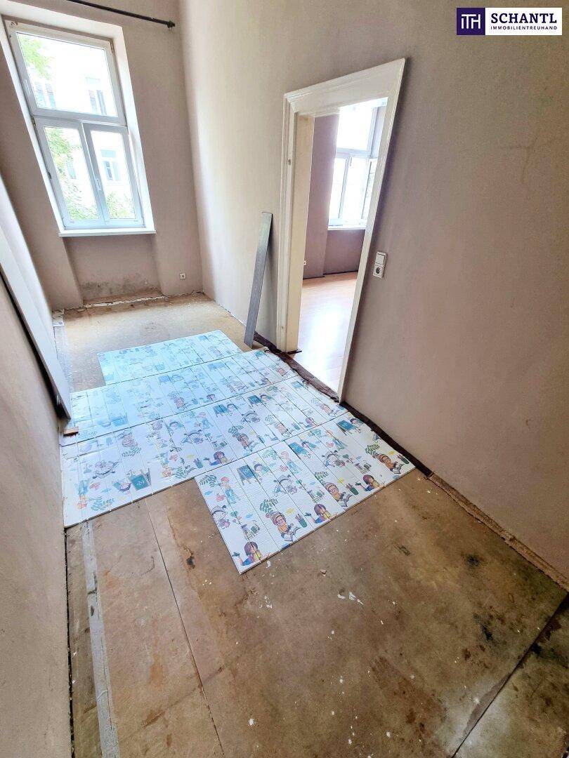 Flur mit Renovierungsbedarf, freigelegtem Boden und Tageslicht durch ein Fenster.