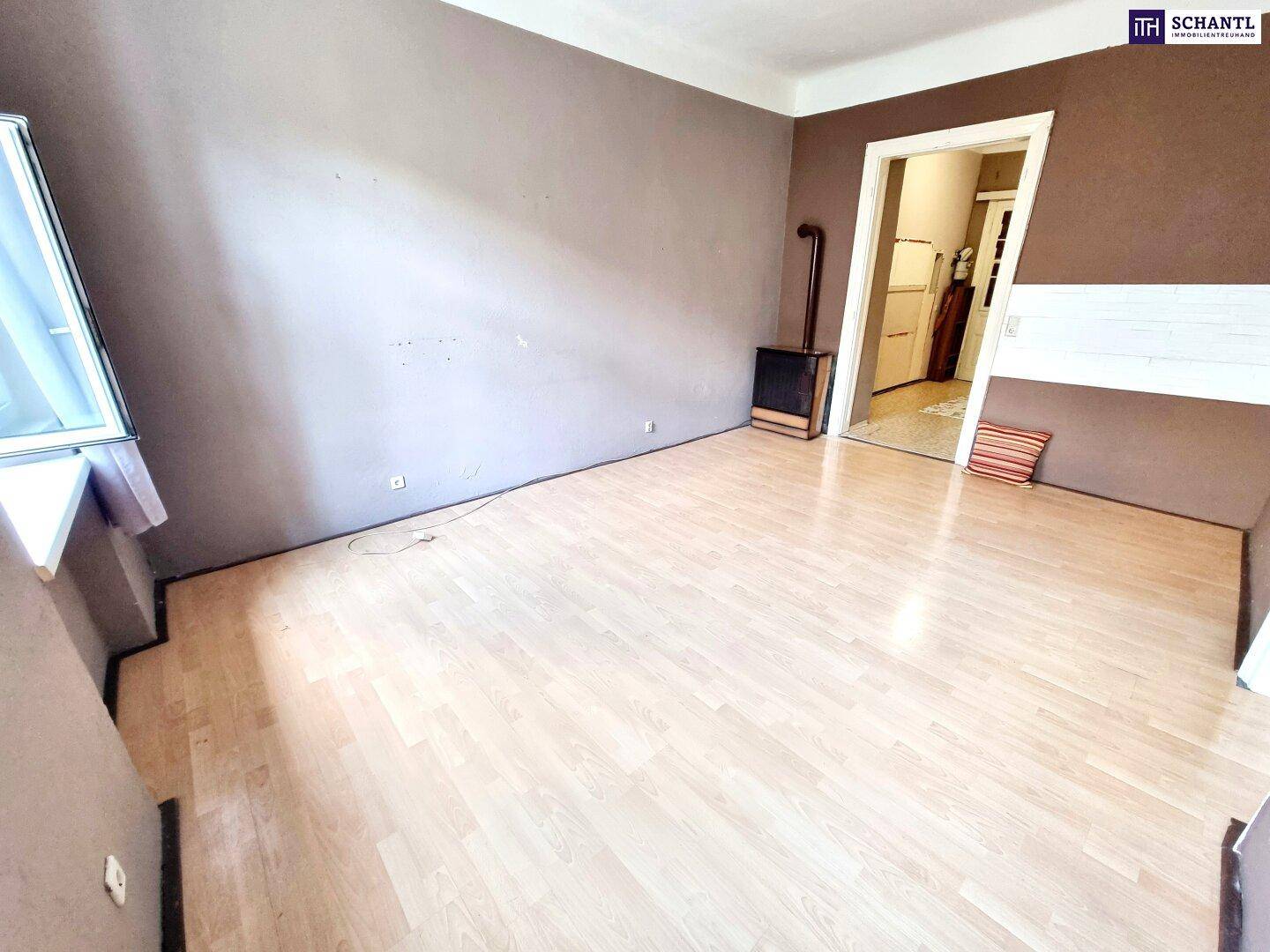 Wohnraum mit Laminatboden, Ofen und einem Fenster, das viel natürliches Licht hereinlässt.