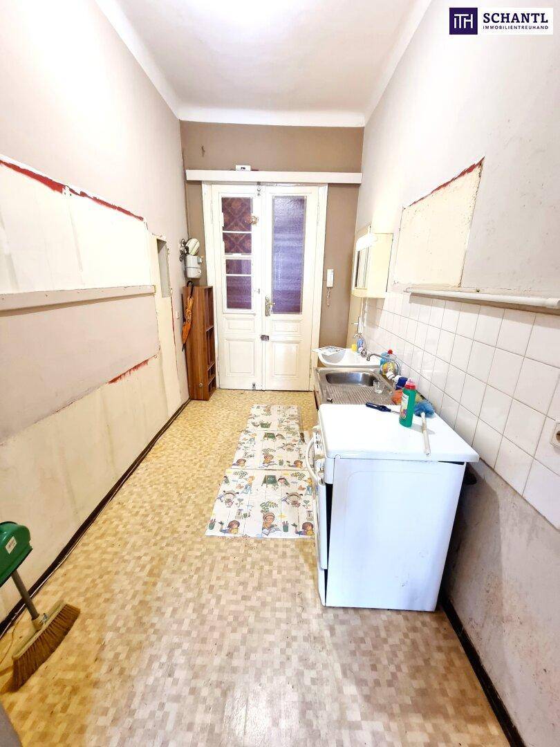 Schmale Küche mit Spülbecken, Fliesenboden und Renovierungsbedarf, mit Zugang nach draußen.
