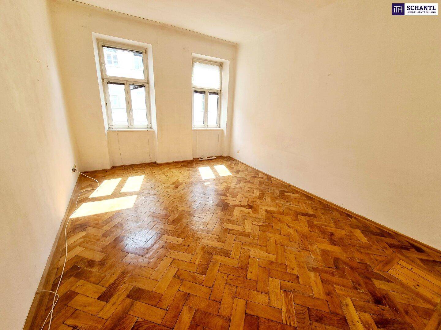 Heller, leerer Raum mit Fischgrätparkett und zwei Fenstern, die viel Tageslicht hereinlassen.