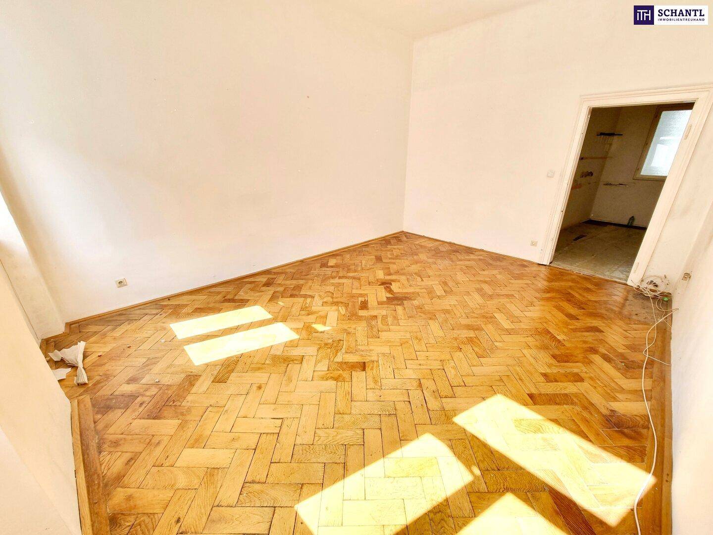 Geräumiger, leerer Raum mit Fischgrätparkettboden und Sonnenlicht, das durch die Fenster fällt.