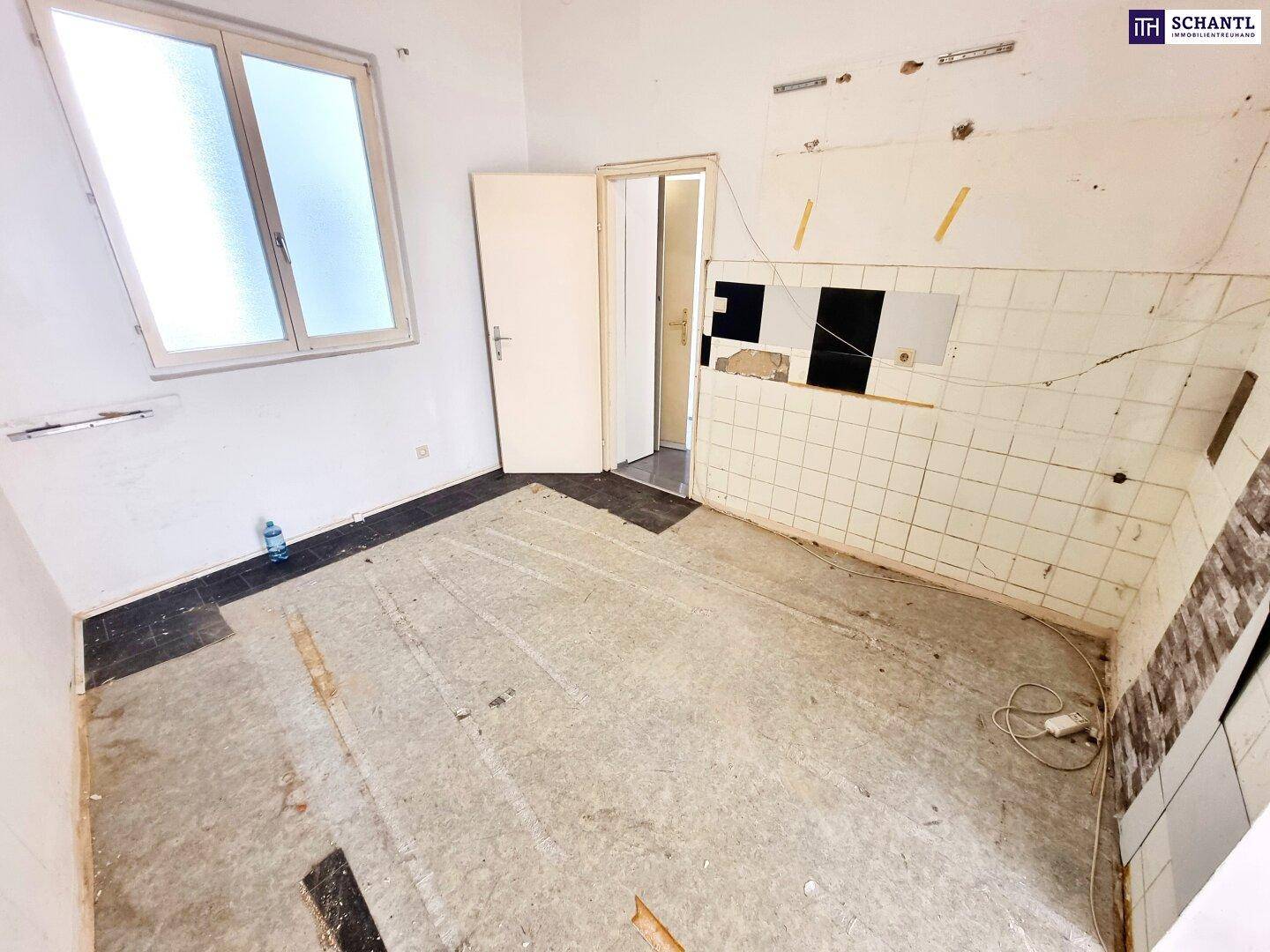 Leere Küche mit alten Wandfliesen und einem Fenster, bereit für eine Renovierung.