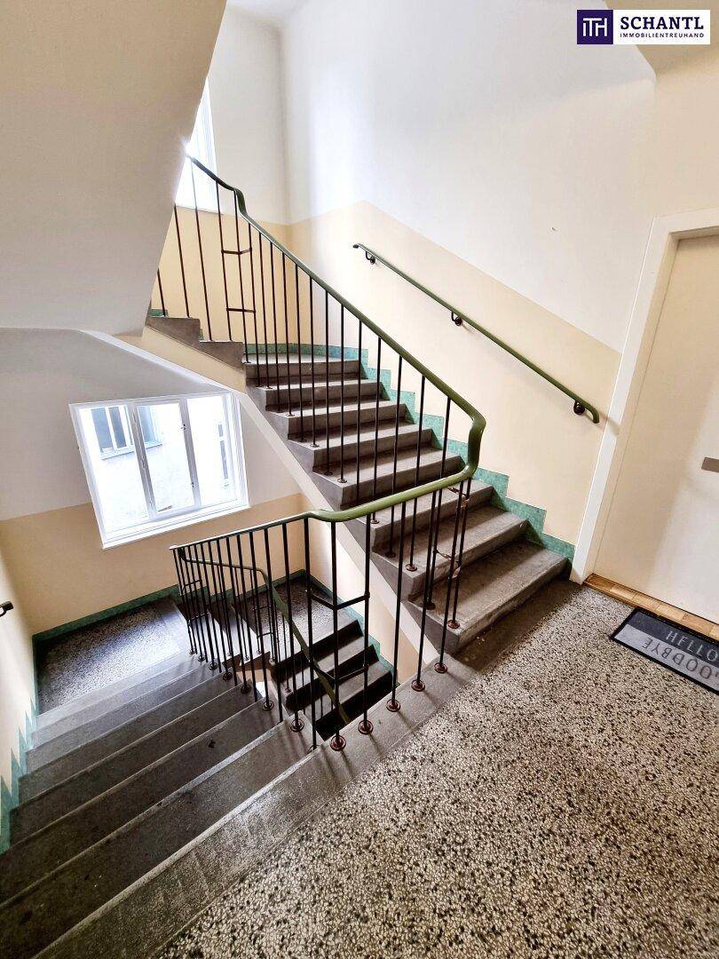Treppenhaus mit Terrazzoboden, Metallgeländer und Fenstern, die Tageslicht hereinlassen.