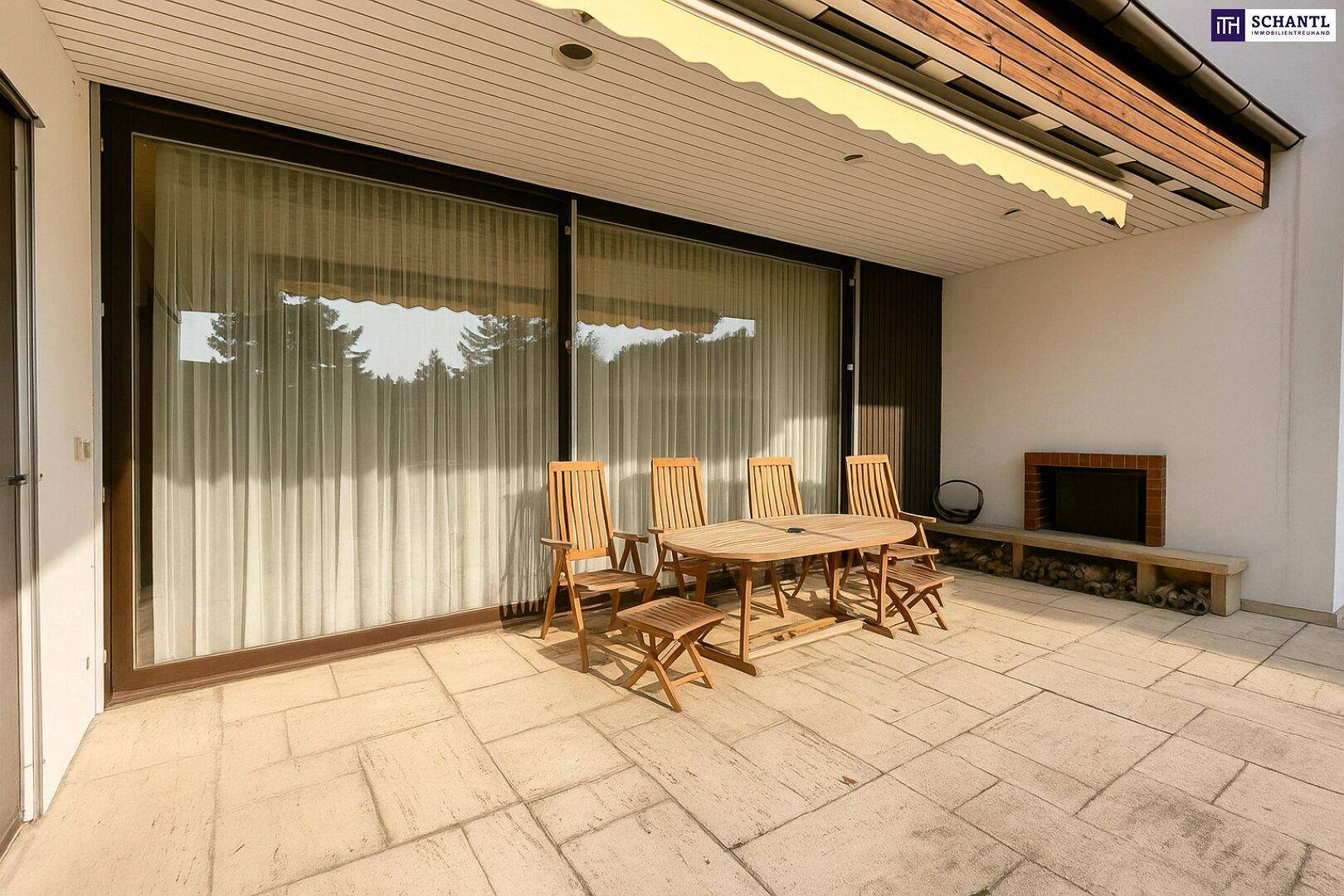 Große Terrasse mit Holzmöbeln, Außenkamin und Blick in den Garten.