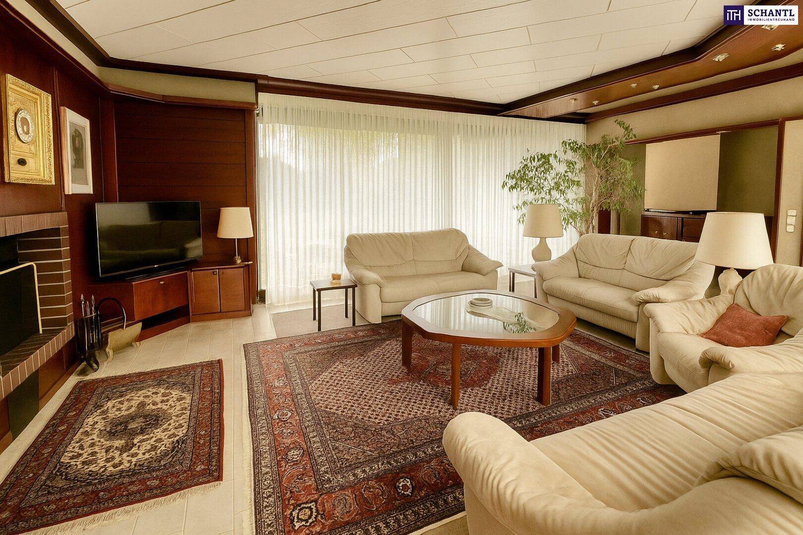 Wohnzimmer mit Kamin, beigen Sofas und großen Fenstern, die viel Licht hereinlassen.