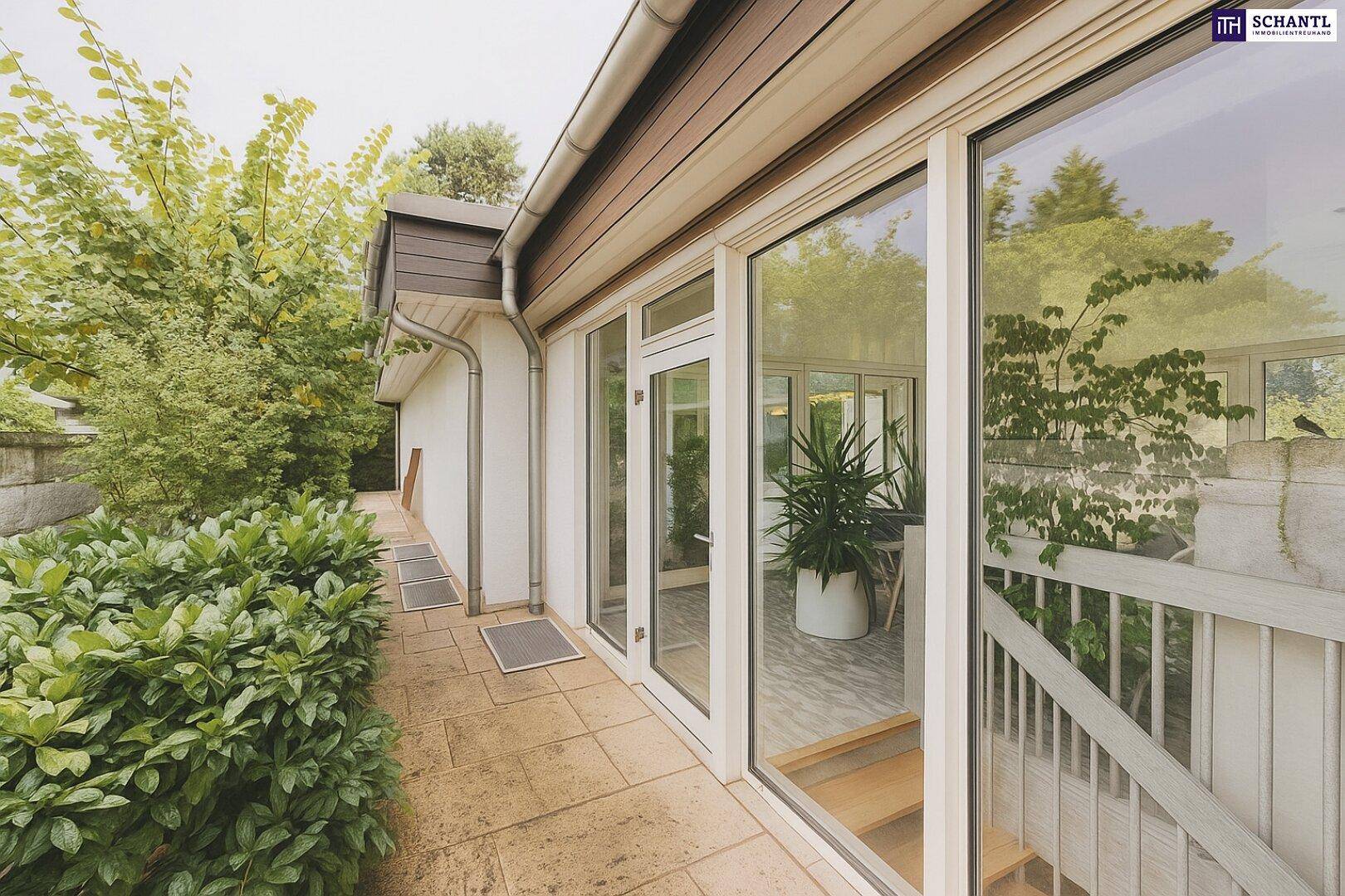 Außenansicht des Wintergartens mit angrenzender Terrasse und üppiger Bepflanzung.
