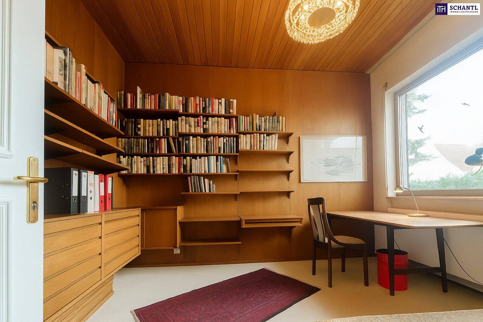 Arbeitszimmer mit umfangreichen Bücherregalen, Schreibtisch und großem Fenster.