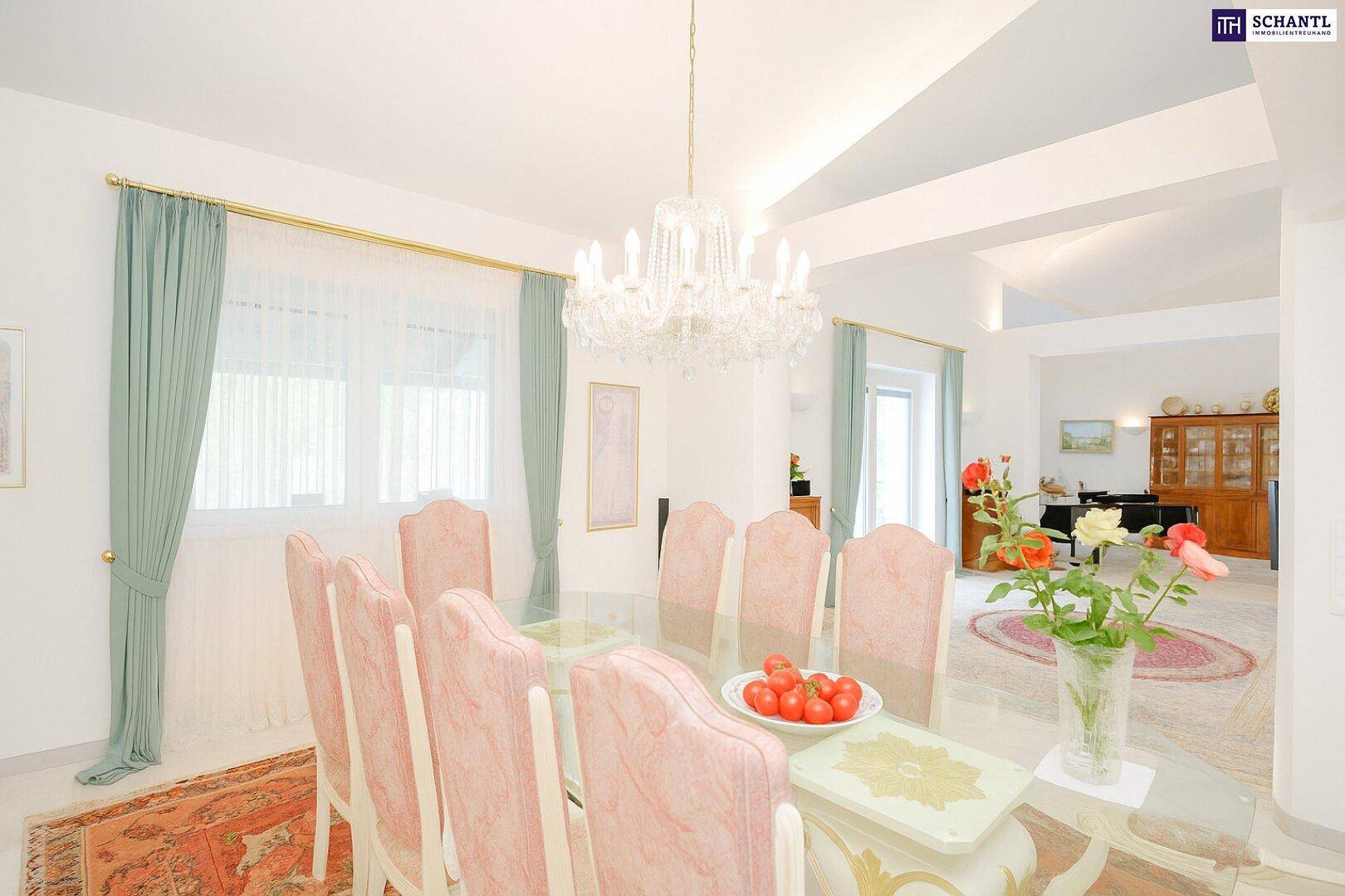 Eleganter Essbereich mit einem großen Glastisch, rosa Stühlen und einem opulenten Kronleuchter, hell und einladend.
