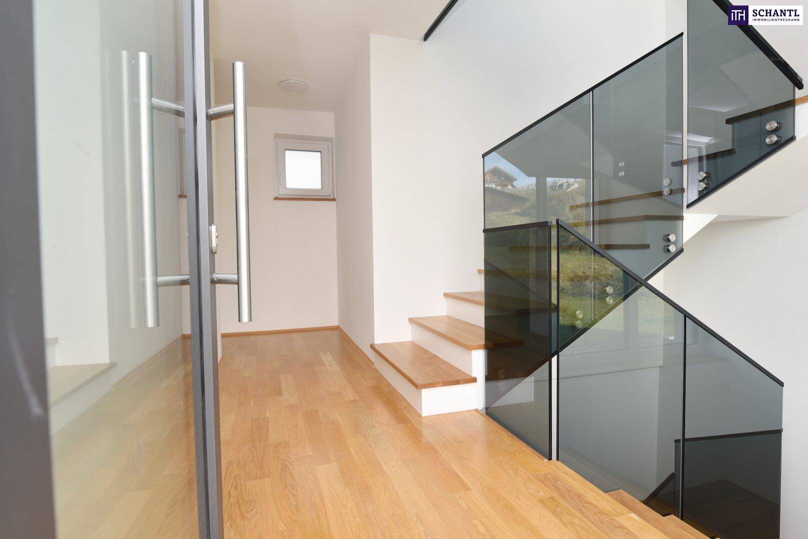 Heller Eingangsbereich mit Holztreppe und moderner Glasbrüstung, die viel Licht hereinlässt.