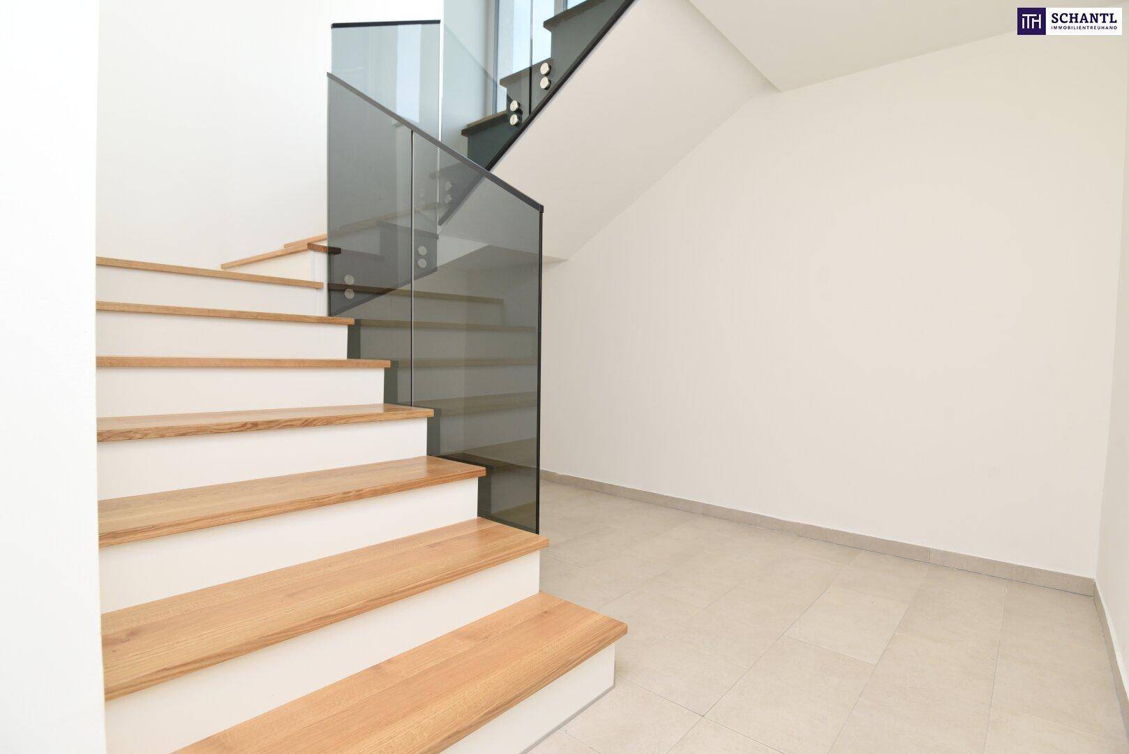 Moderne Treppe mit Holzstufen und Glasgeländer in einem hellen Eingangsbereich.