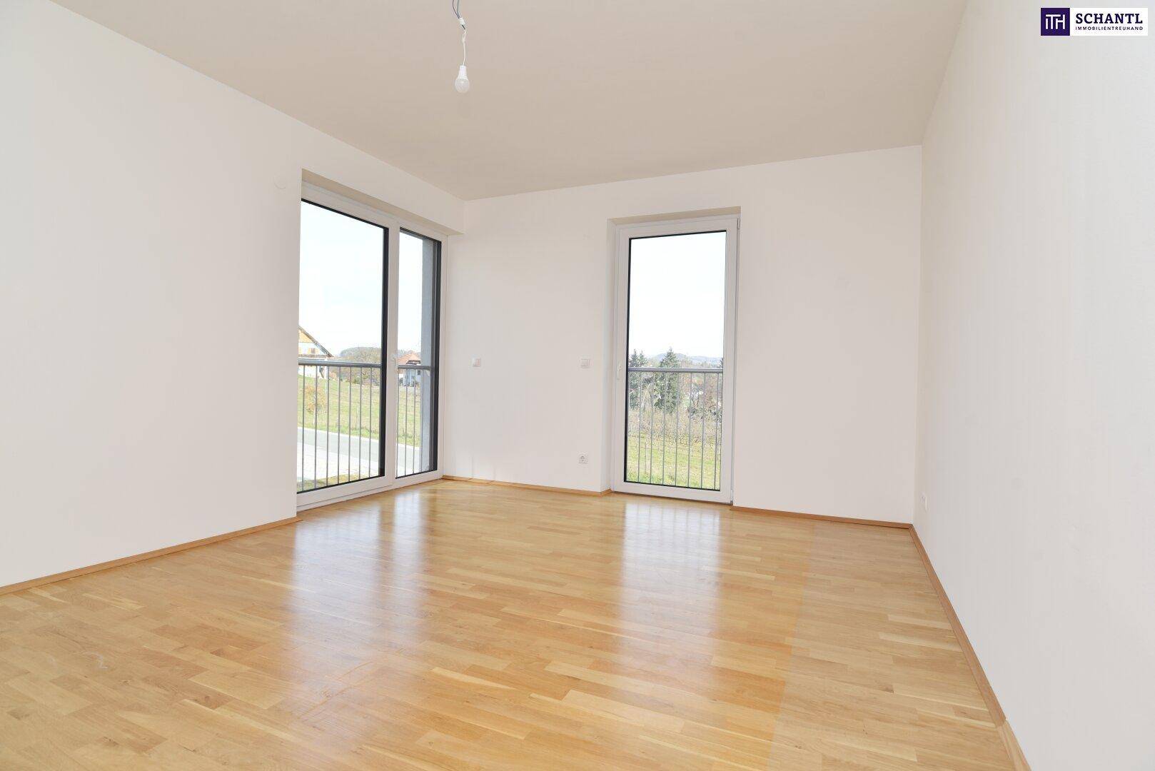 Helles, leeres Zimmer mit Parkettboden und zwei Fenstern mit französischem Balkon.