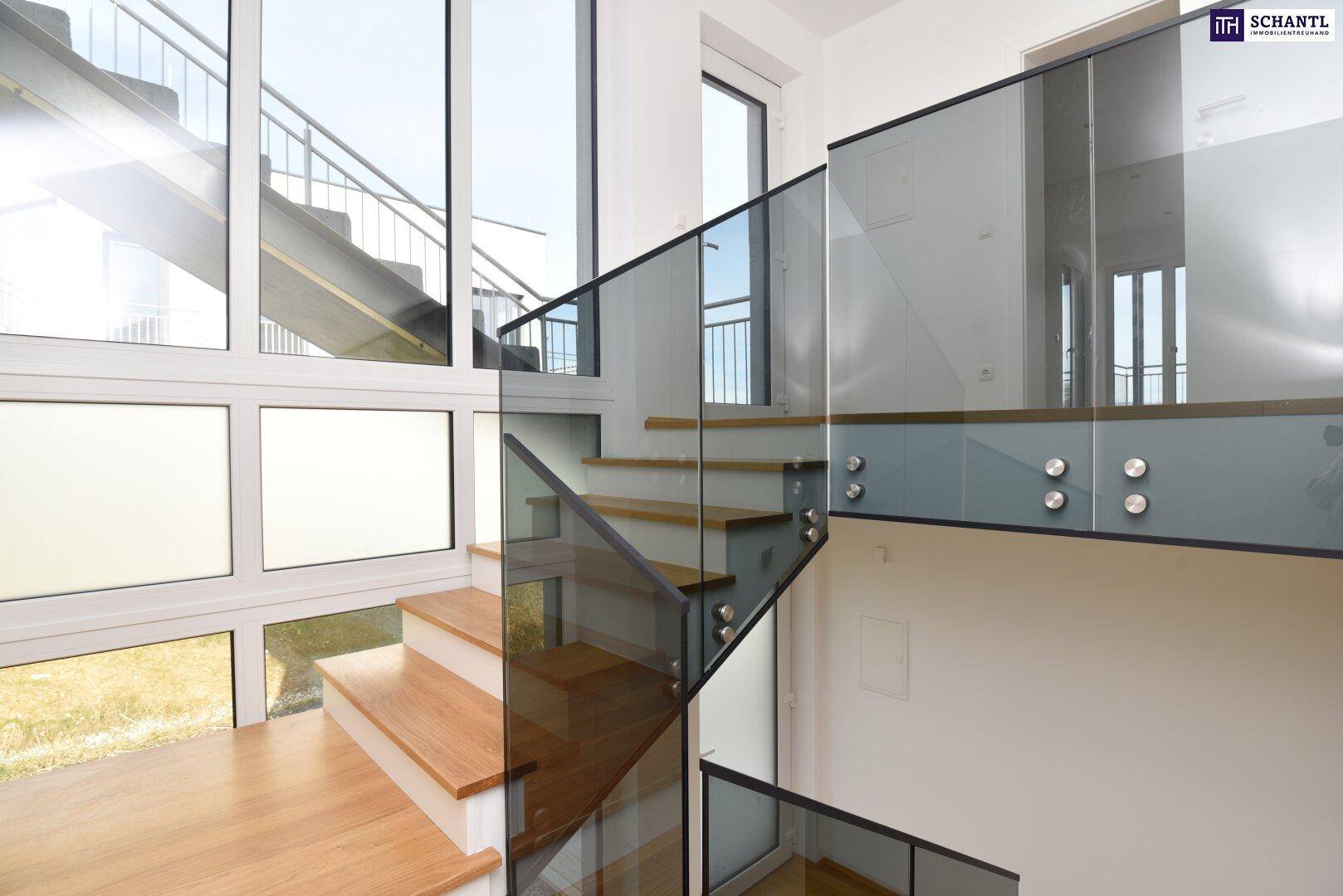 Moderne Treppe mit Glasgeländer und großen Fenstern, die den Raum mit Licht durchfluten.