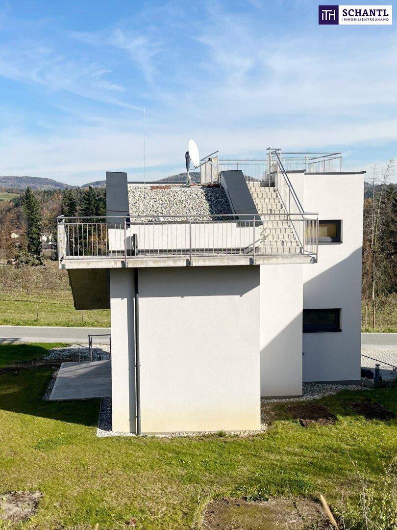Modernes Gebäude mit Flachdach und Dachterrasse, umgeben von grüner Landschaft.