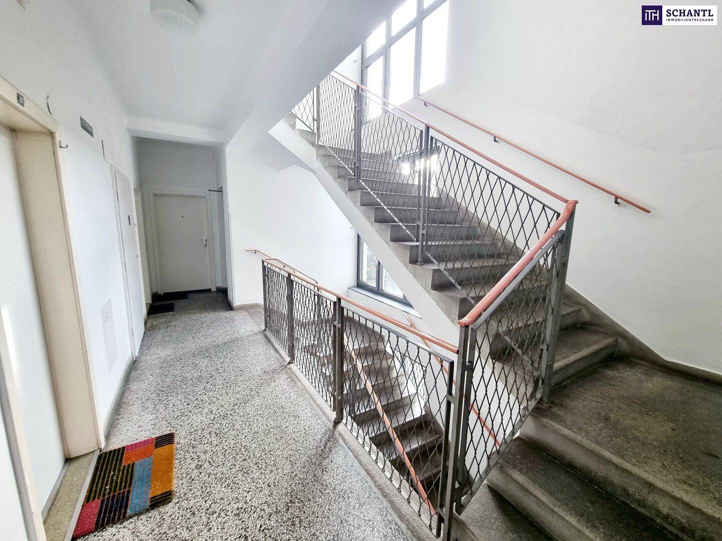 Treppenhaus eines Wohngebäudes mit Terrazzoboden und Metallgeländer.