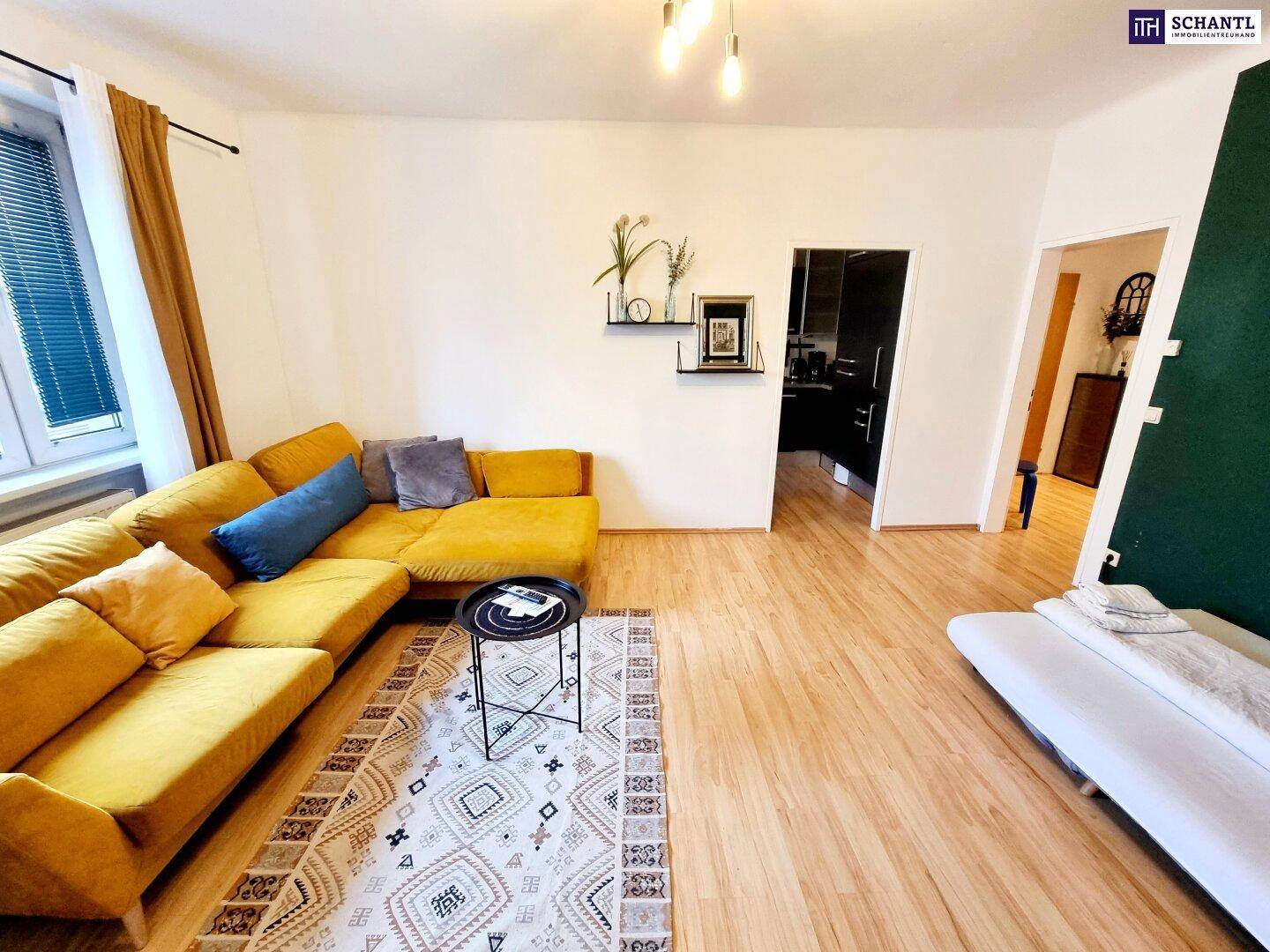 Helles Wohnzimmer mit gelbem Ecksofa, Holzboden und Blick in den Flur.