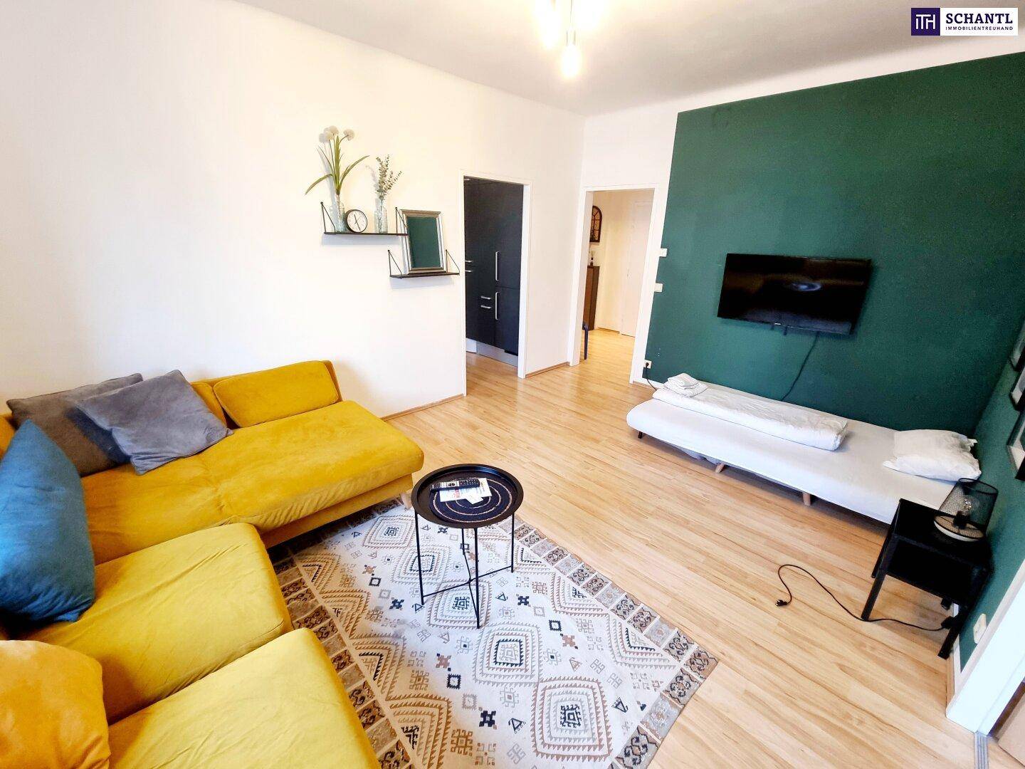 Gemütliches Wohnzimmer mit gelbem Sofa, Holzboden und einem Fernseher an der dunkelgrünen Wand.