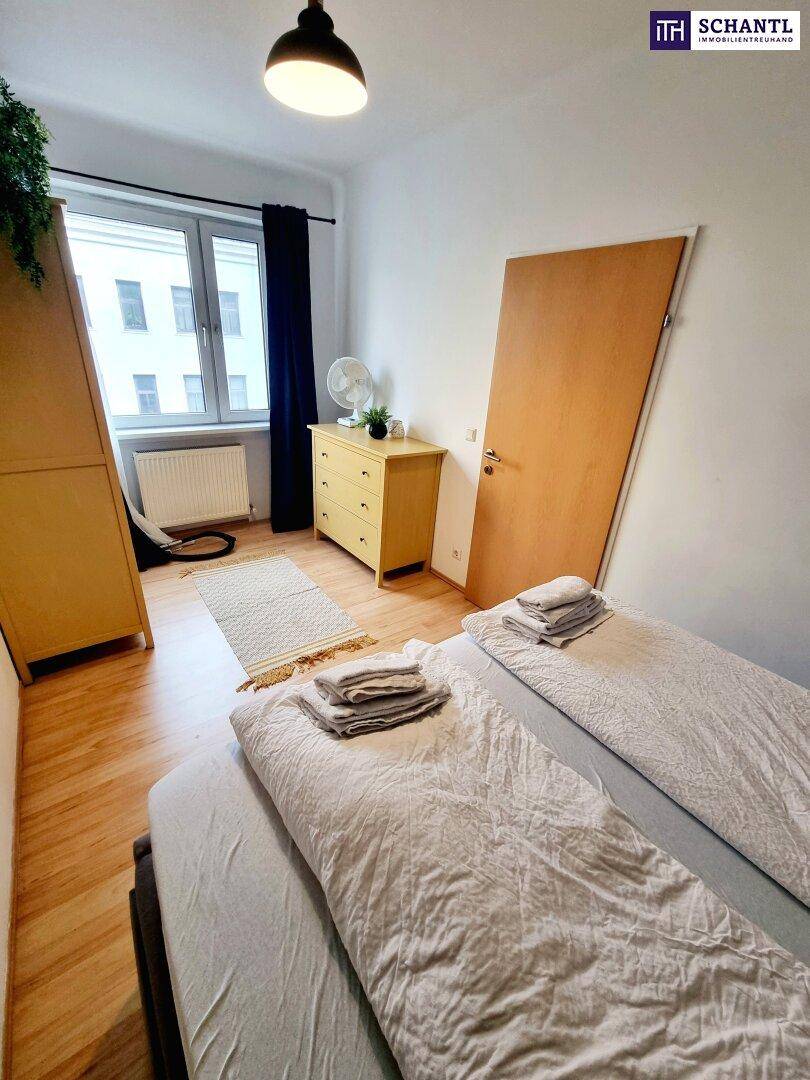 Schlafzimmer mit Doppelbett, Kommode und Fenster, das viel Tageslicht hereinlässt.
