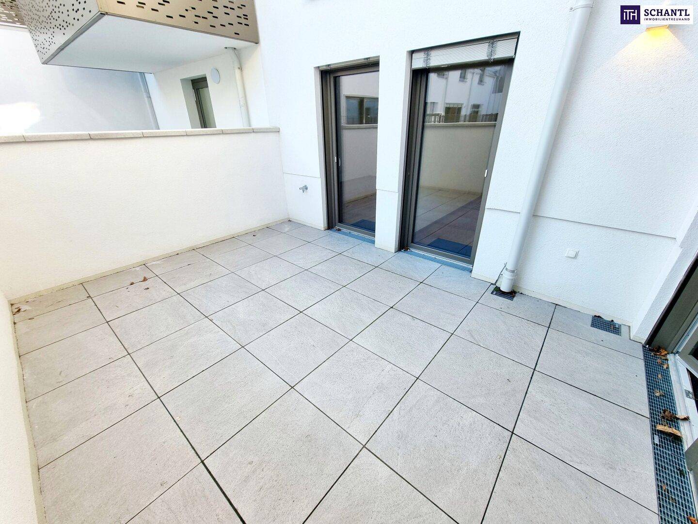 Geräumige Terrasse mit hellen Fliesen und Zugang zu den Innenräumen durch große Glastüren.