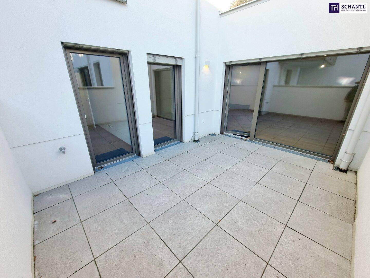 Geräumige Terrasse mit hellen Fliesen und Zugang zu den Innenräumen durch große Glastüren.