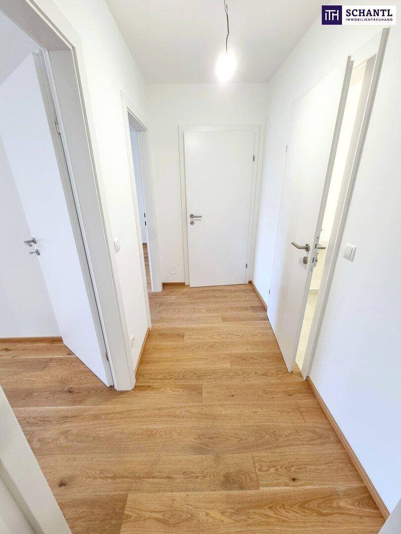 Langer, heller Flur mit Parkettboden und mehreren weißen Türen.