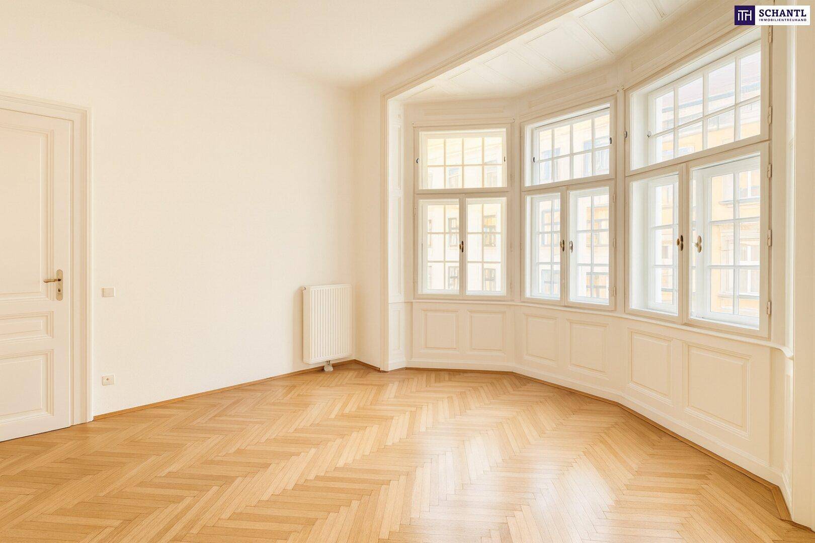 Geräumiges Zimmer mit hellem Fischgrätparkett, hohen Decken und einem Erkerfenster.