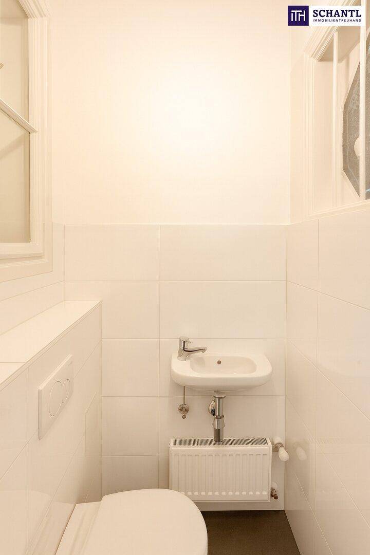 Kleines Gäste-WC mit weißen Fliesen, wandhängender Toilette und einem kleinen Waschbecken.