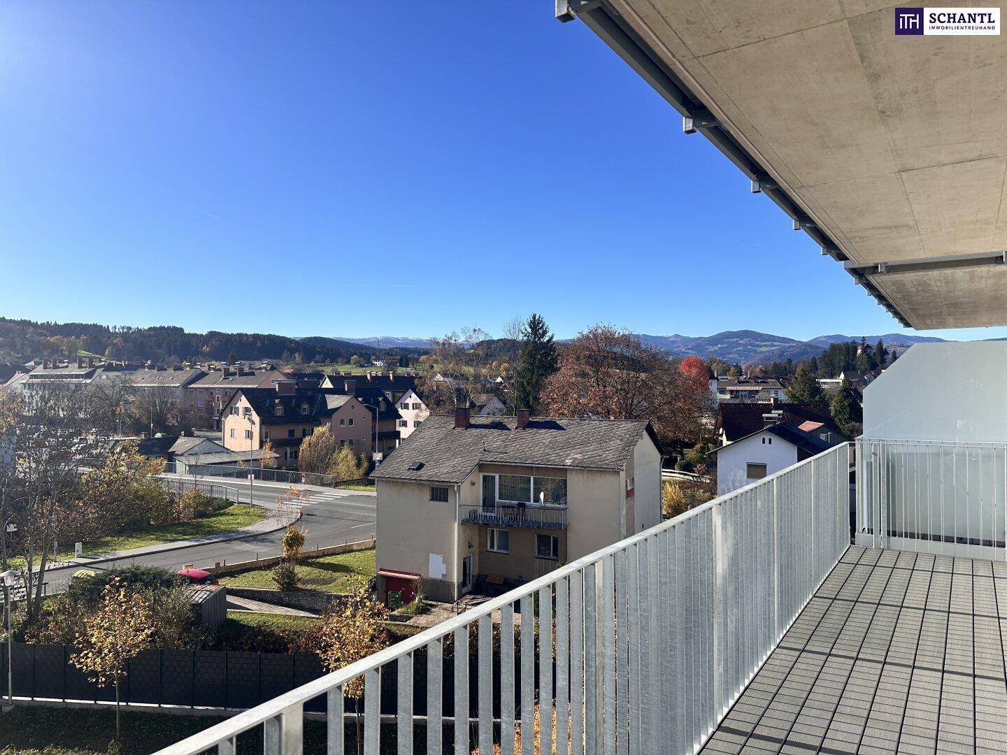 Weitläufiger Ausblick vom Balkon über eine Wohnsiedlung und die umliegende grüne Hügellandschaft.