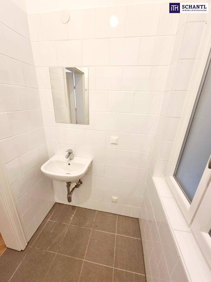 Funktionales Badezimmer mit Einzelwaschbecken, Spiegel und weißen Fliesen, ergänzt durch ein Fenster.