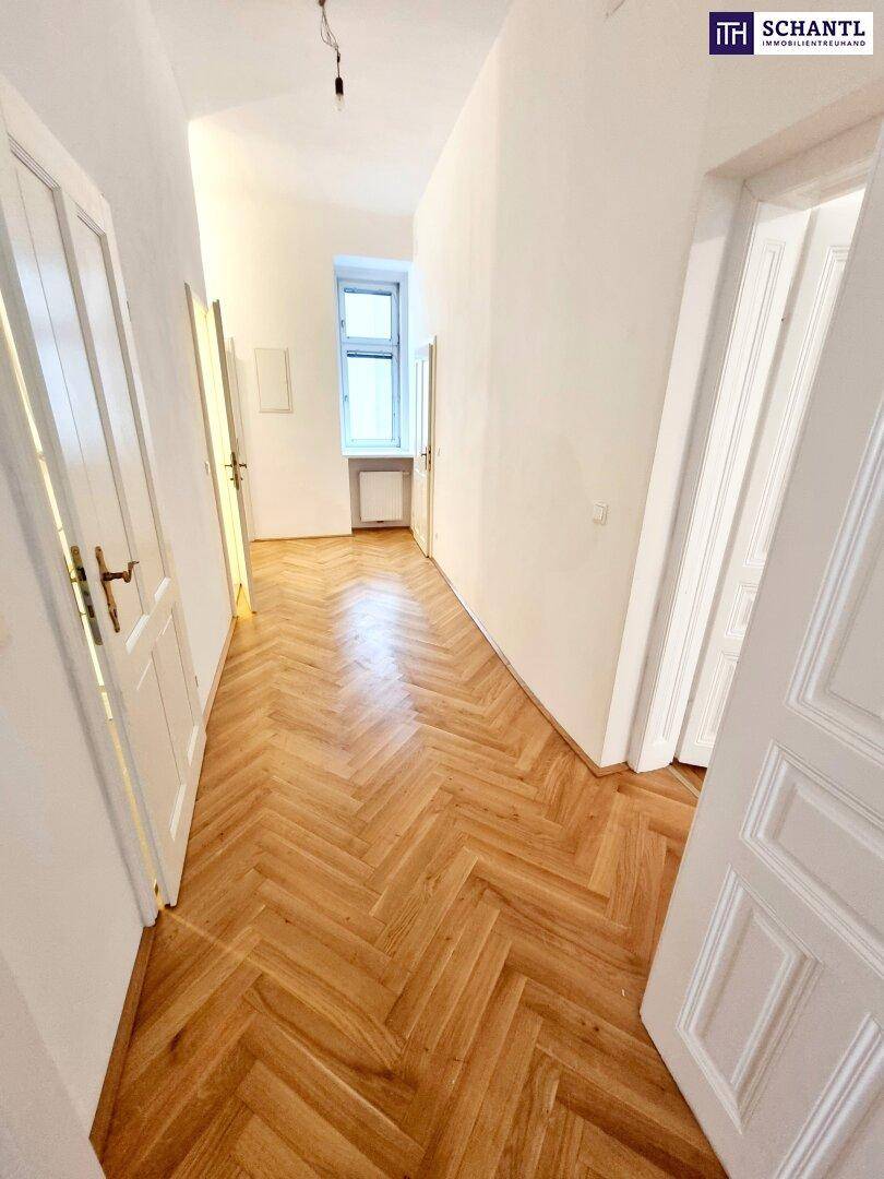 Langer, heller Flur mit Fischgrätparkett und einem Fenster am Ende, das für natürliches Licht sorgt.