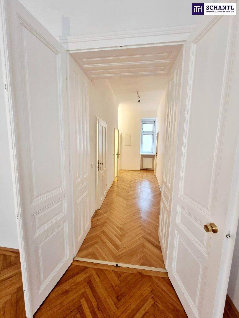 Blick durch offene Flügeltüren in einen langen Flur mit elegantem Fischgrätparkett und hohen Decken.