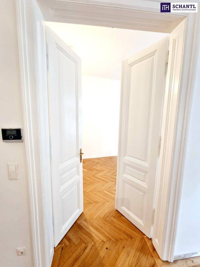 Offene Flügeltüren geben den Blick frei auf einen hellen Raum mit klassischem Fischgrätparkett.