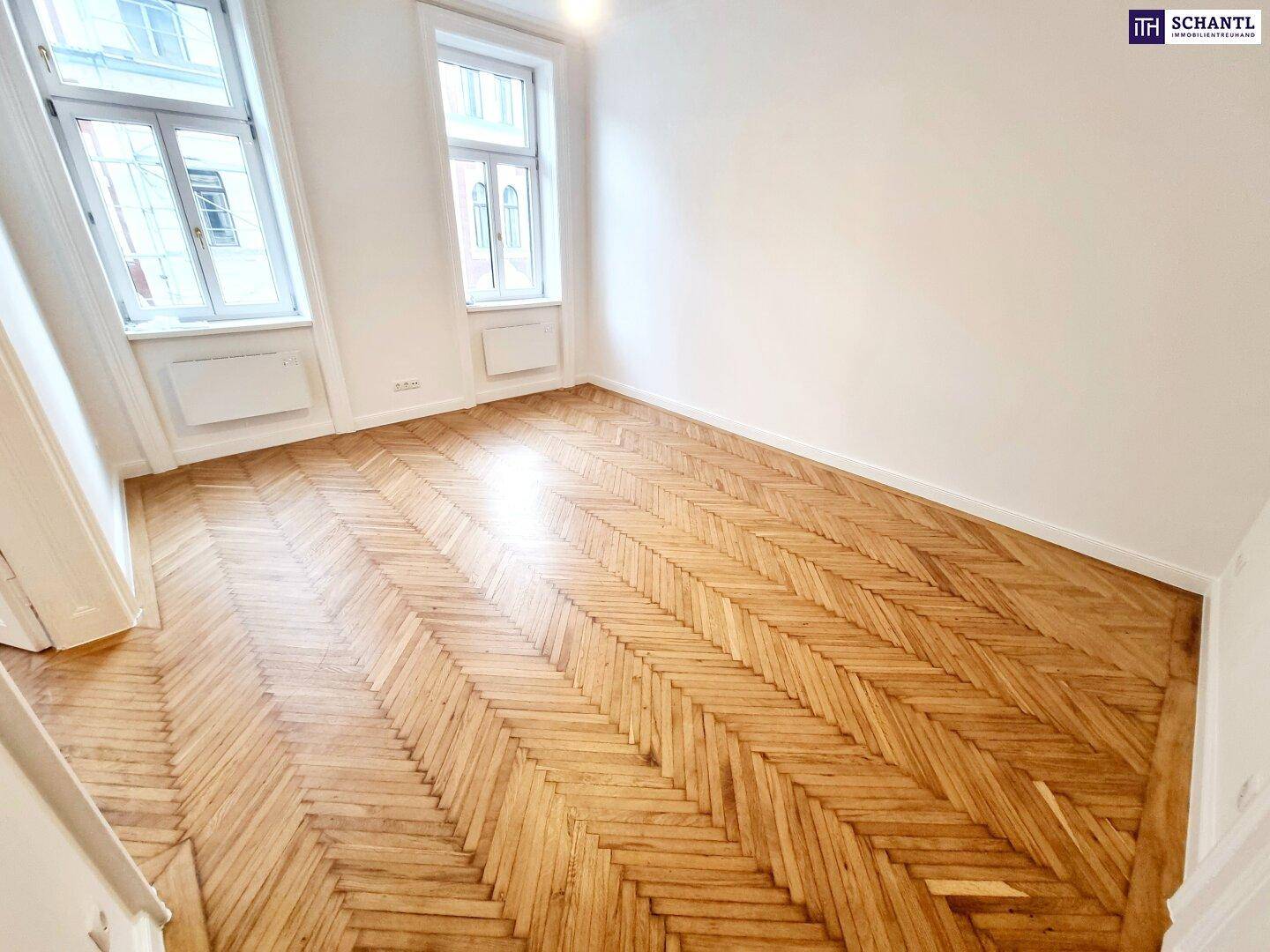 Lichtdurchflutetes Zimmer mit Fischgrätparkett und großen Fenstern, ideal für Wohnzwecke.