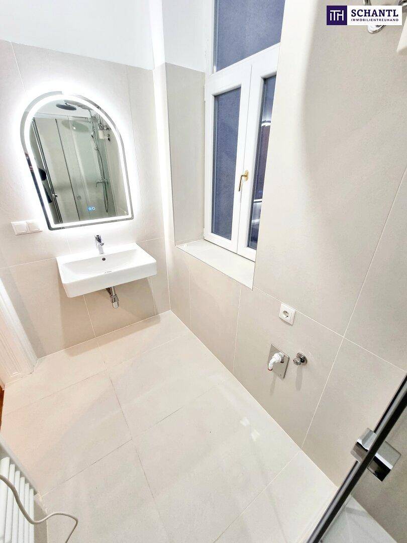 Modernes Badezimmer mit hellen Fliesen, beleuchtetem Spiegel und ebenerdiger Dusche.