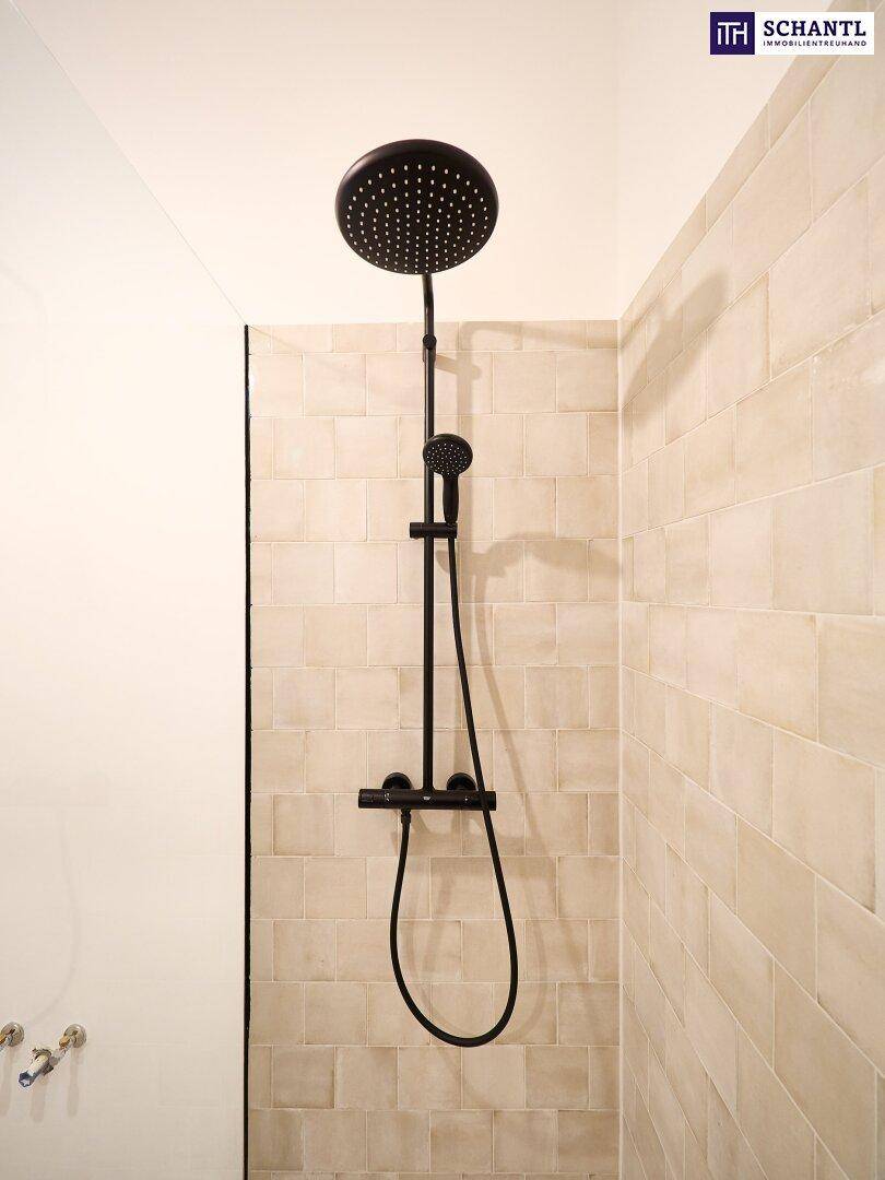 Moderne Duschkabine mit schwarzen Armaturen und beigefarbenen Fliesen an der Wand.