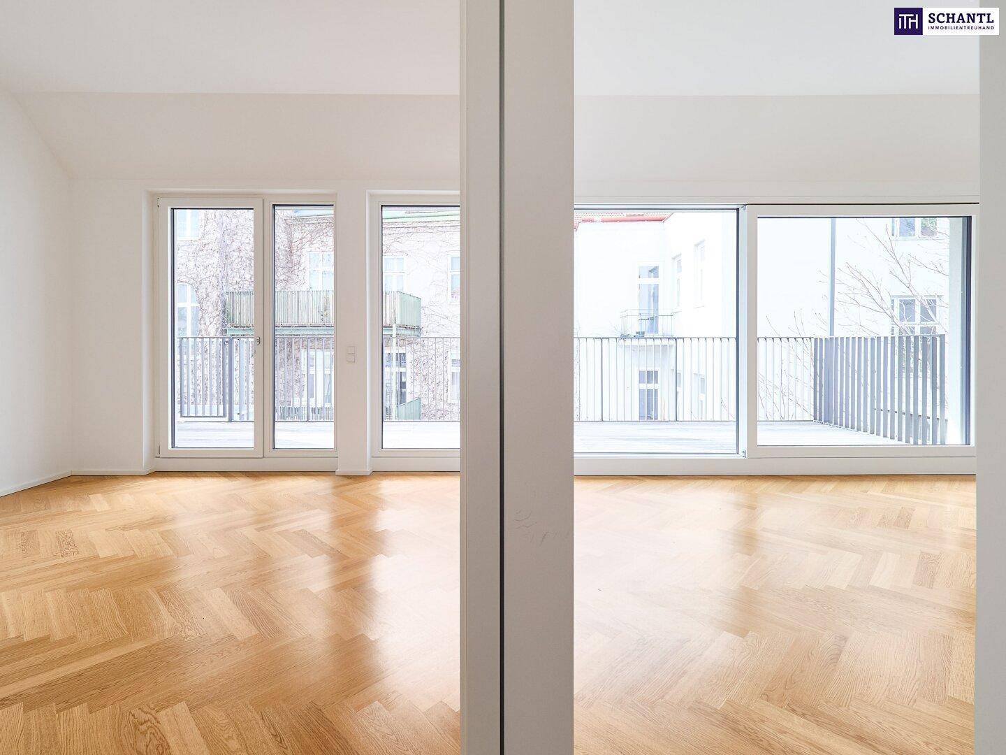 Heller Raum mit Fischgrätparkett und großen Fenstern, die zu einem Balkon führen.