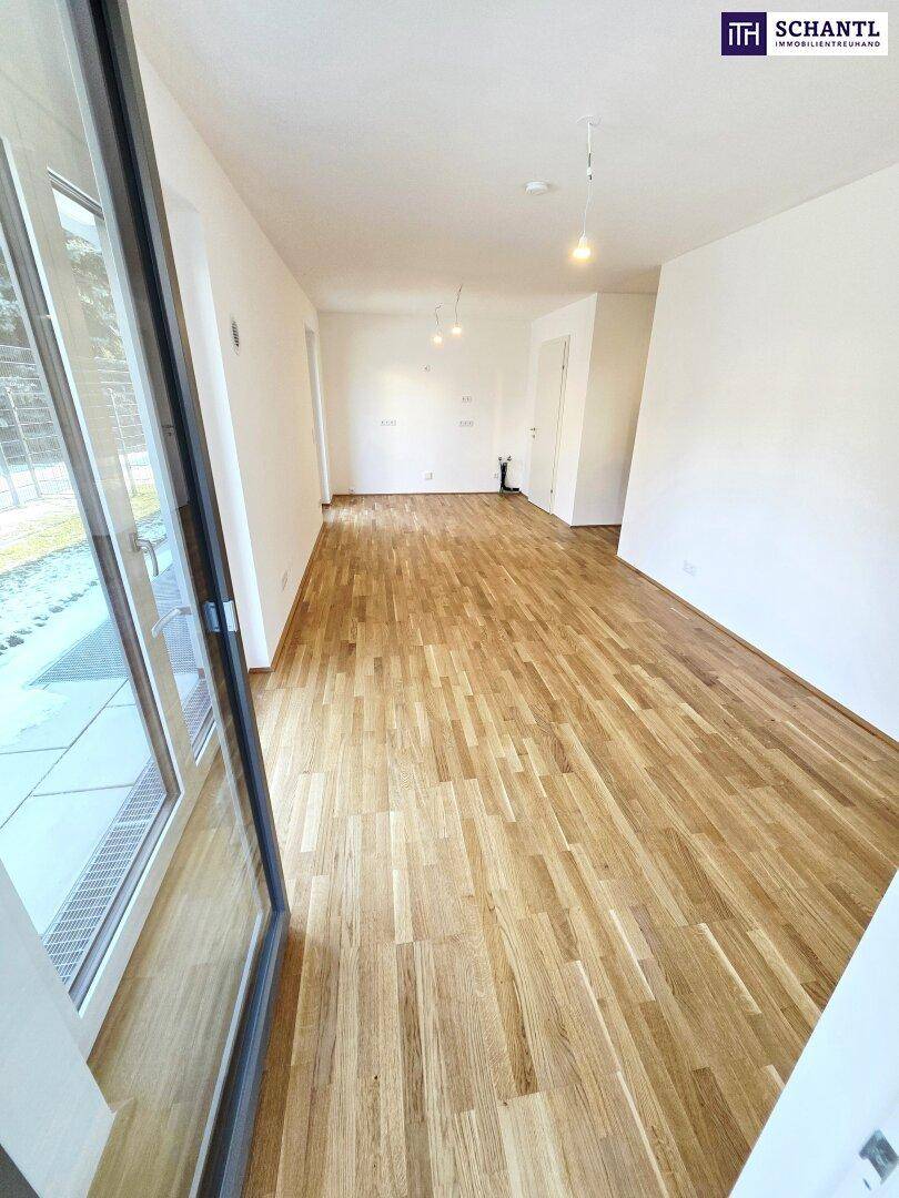 Heller, leerer Wohnbereich mit neuem Parkettboden und großem Fenster mit Zugang zum Außenbereich.