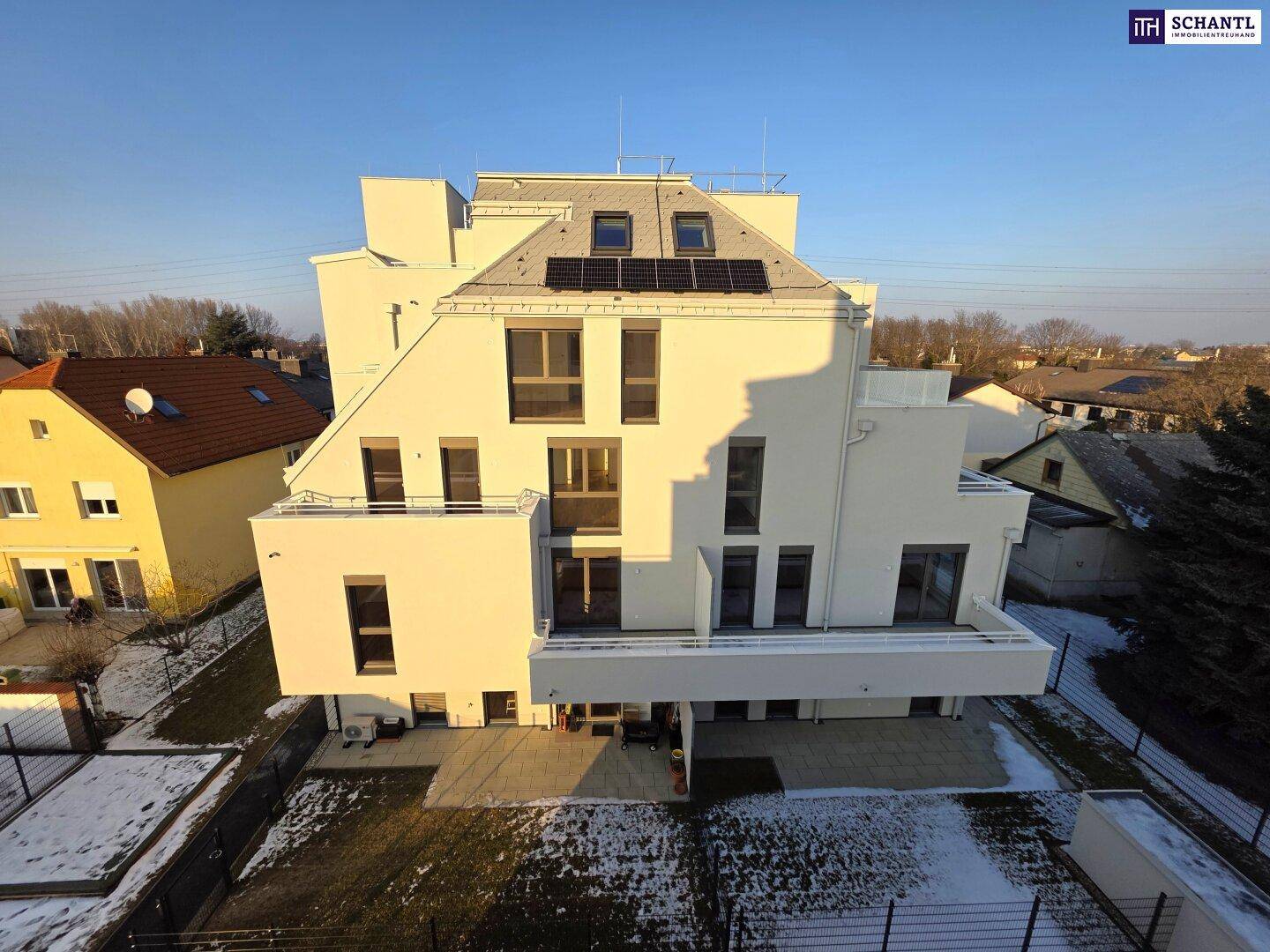 Dachansicht des modernen Gebäudes mit Photovoltaikanlage und umliegenden Wohnhäusern.