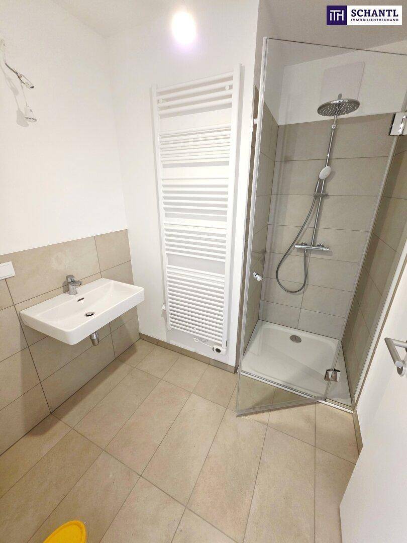 Modernes Badezimmer mit Dusche, Waschbecken und beheiztem Handtuchhalter, in hellen Farbtönen gehalten.