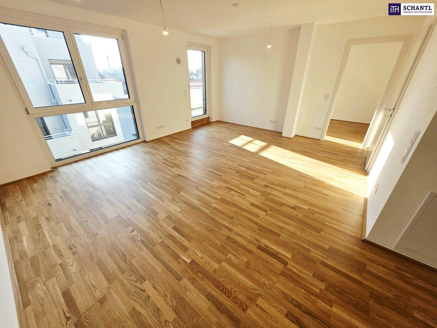 Helles, leeres Zimmer mit modernem Parkettboden und großen Fenstern, die viel Tageslicht hereinlassen.