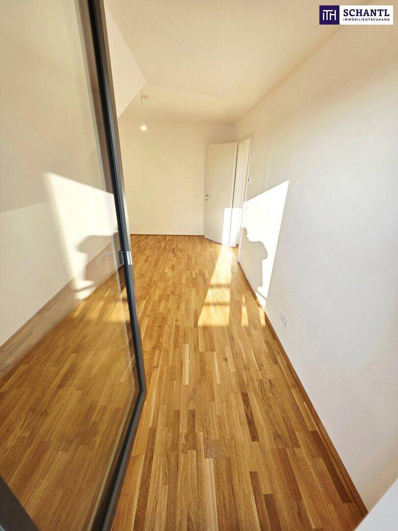 Geräumiger, heller Raum mit Holzboden und großen Fenstern, die viel Tageslicht hereinlassen.