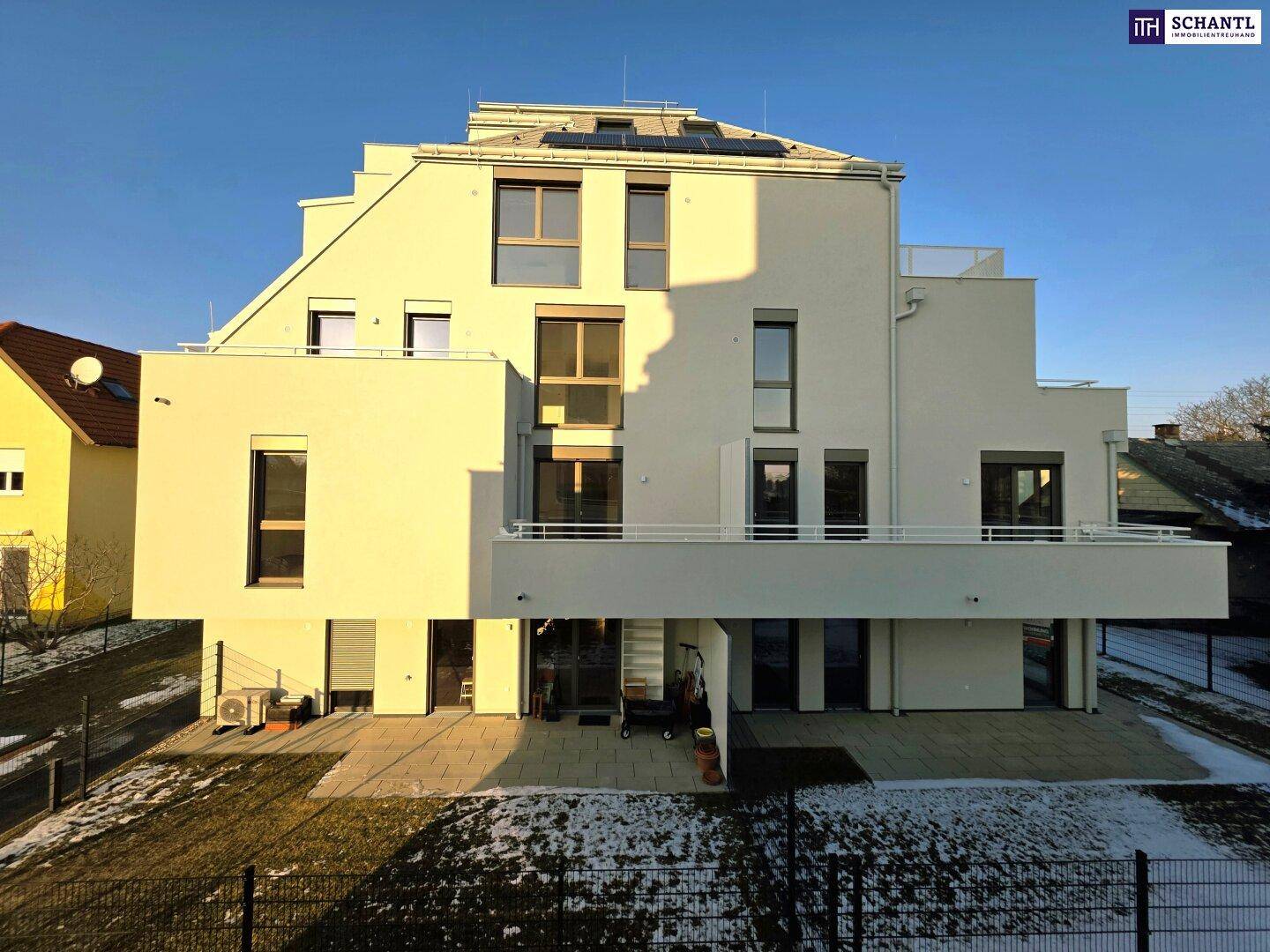 Moderne Gebäudefassade mit Terrassenbereich und Garten im Winter, umgeben von Schnee.