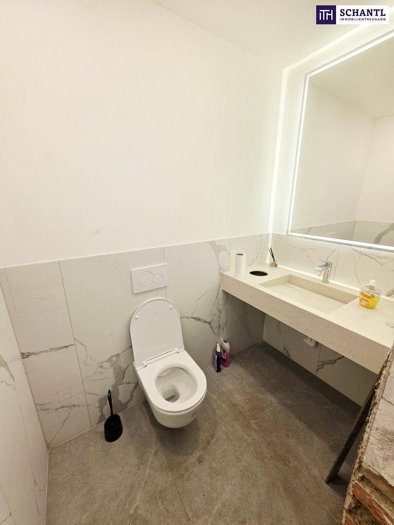 Modernes WC mit wandhängender Toilette, Marmorfliesen und beleuchtetem Spiegel.