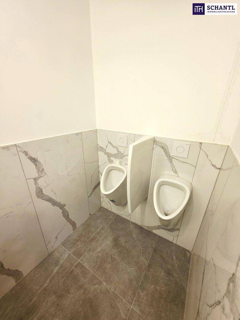 Moderner Toilettenraum mit zwei Urinalen und Marmorfliesen an den Wänden.