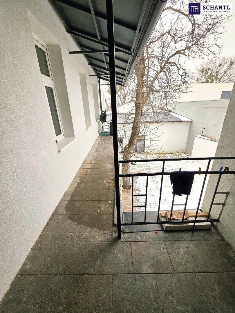 Langer, überdachter Balkon mit Steinplattenboden und Blick auf den Innenhof.