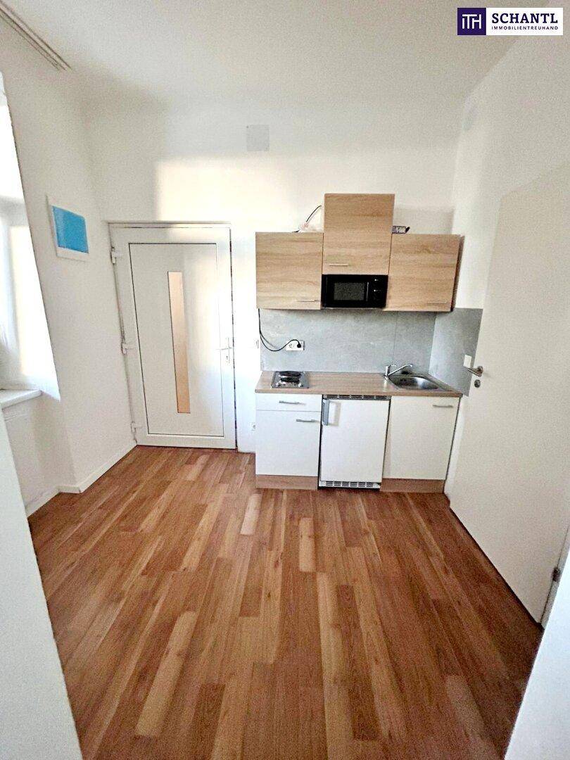 Kleiner Raum mit integrierter Küchenzeile, Holzboden und hellem Fenster.