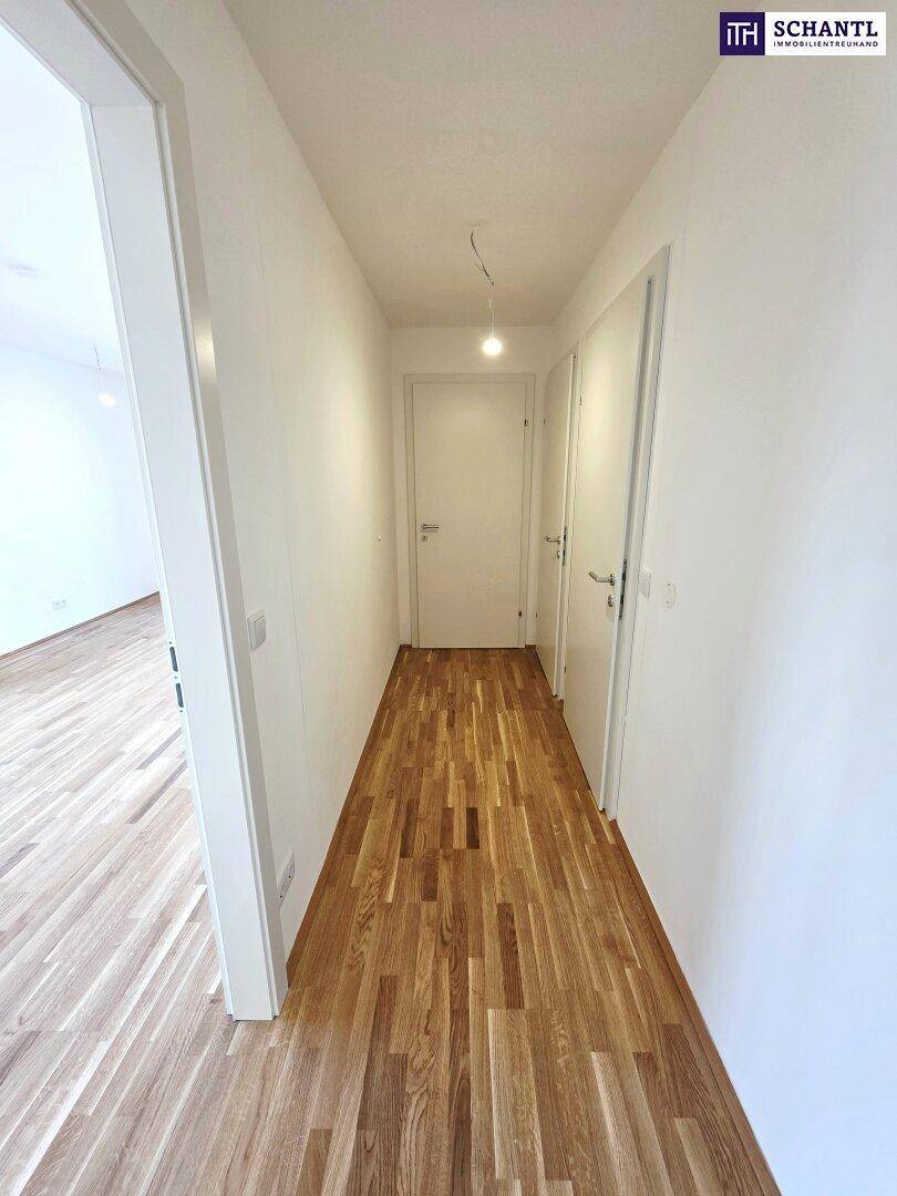 Heller Flur mit Holzboden und weißen Wänden, der zu weiteren Räumen führt.