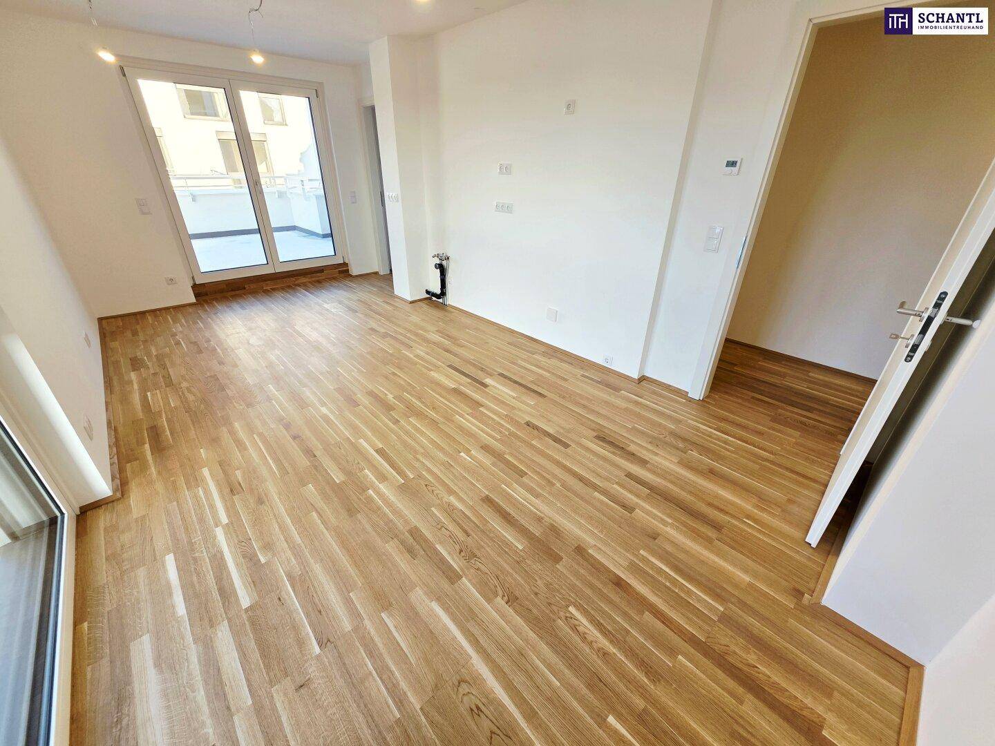 Leerer Raum mit Holzboden und Zugang zu einem Balkon, der viel Tageslicht hereinlässt.