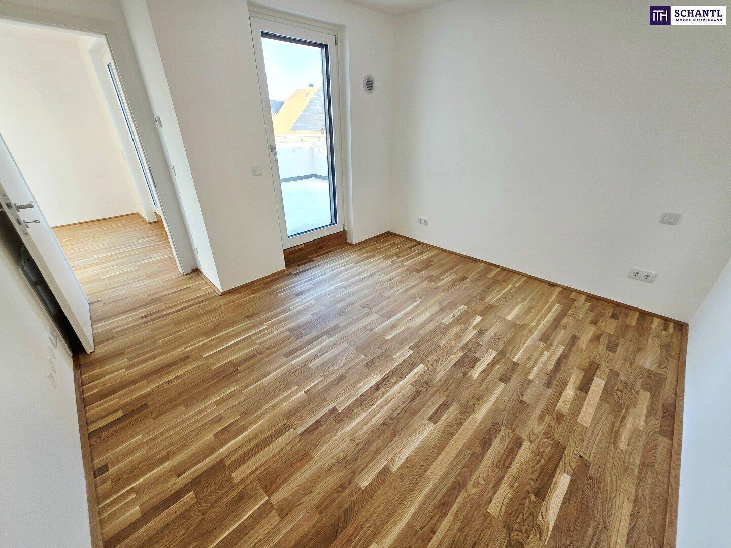 Heller Raum mit Holzboden und großem Fenster, das einen Ausblick auf die Umgebung bietet.